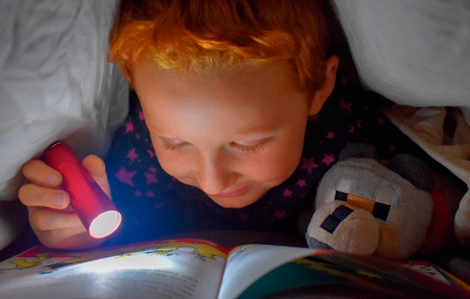 Ребенок читает книгу под одеялом с фонариком